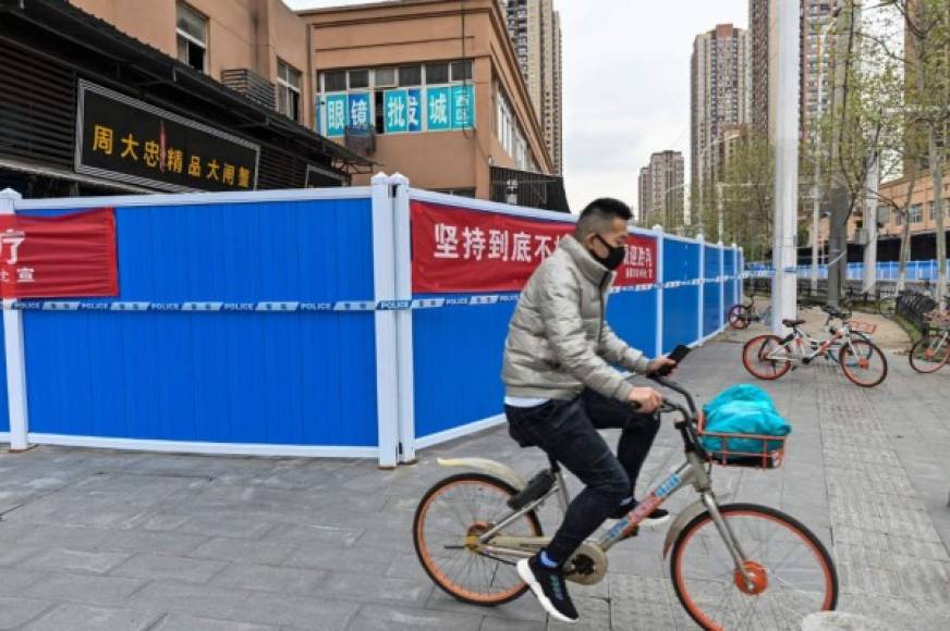 People, wearing face masks as a preventive measure against the spread of the COVID-19 novel coronavirus, are seen on a street in a neighborhood closed off by barriers in Wuhan, China's central Hubei province on April 20, 2020. - China's economy shrank for the first time in decades last quarter as the coronavirus paralysed the country, in a historic blow to the Communist Party's pledge of continued prosperity in return for unquestioned political power. The main access to the neighbourhood is on another street where workers take the temperatures of people and maintain the Wuhan health code. (Photo by Hector RETAMAL / AFP)