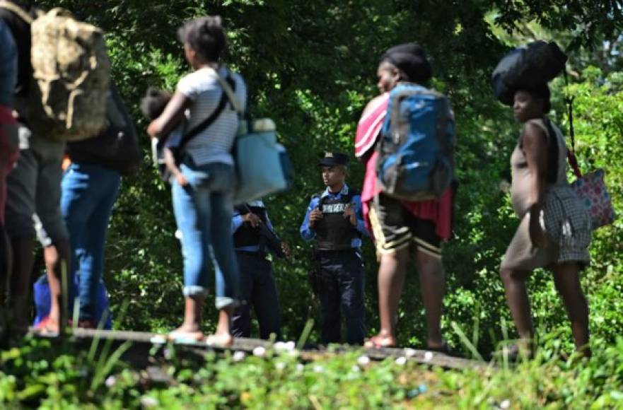 Los oficiales de policía vigilan mientras los migrantes africanos y haitianos permanecen al costado de una carretera después de pasar por un 'cruce ciego' de Nicaragua a Honduras en su camino a los Estados Unidos, en Guasaule, Honduras, el 16 de noviembre de 2019.