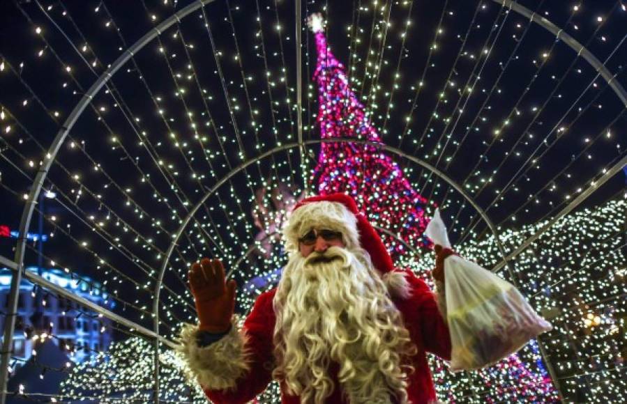 Un hombre disfrazado de Papa Noel saluda a los fotógrafos delante del árbol navideño que decora la plaza central de Skopie, Macedonia.
