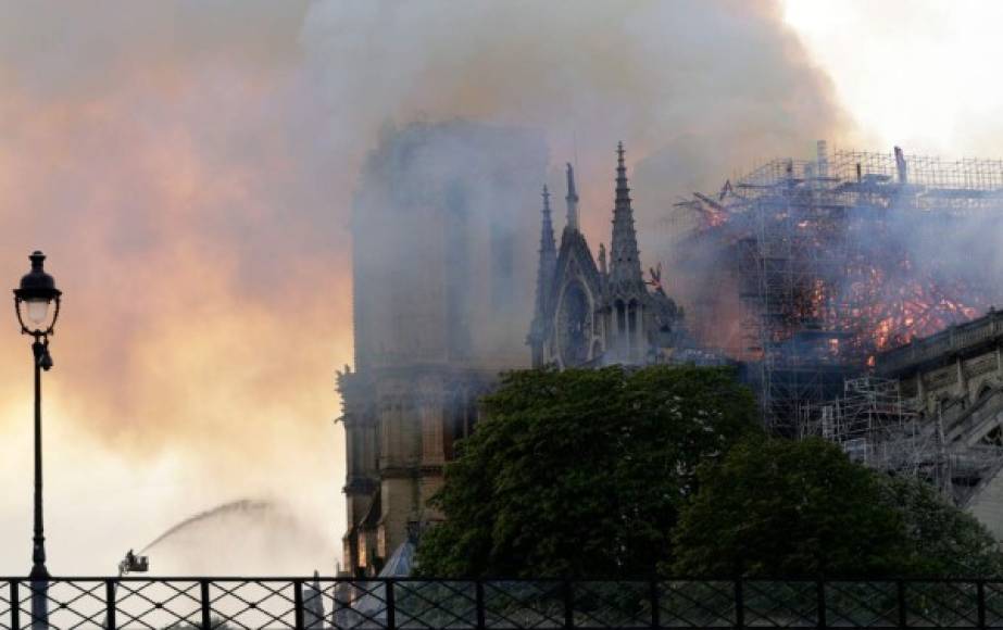 Un bombero usa una manguera para apagar las llamas y el humo que sale del techo de la catedral de Notre-Dame.