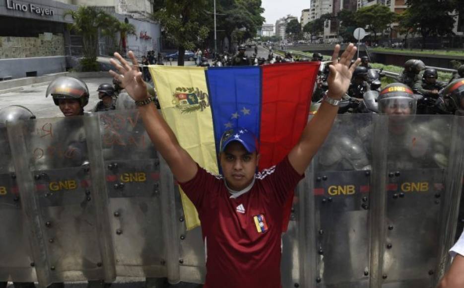 Un venezolano levanta la Bandera ante un contingente policial.