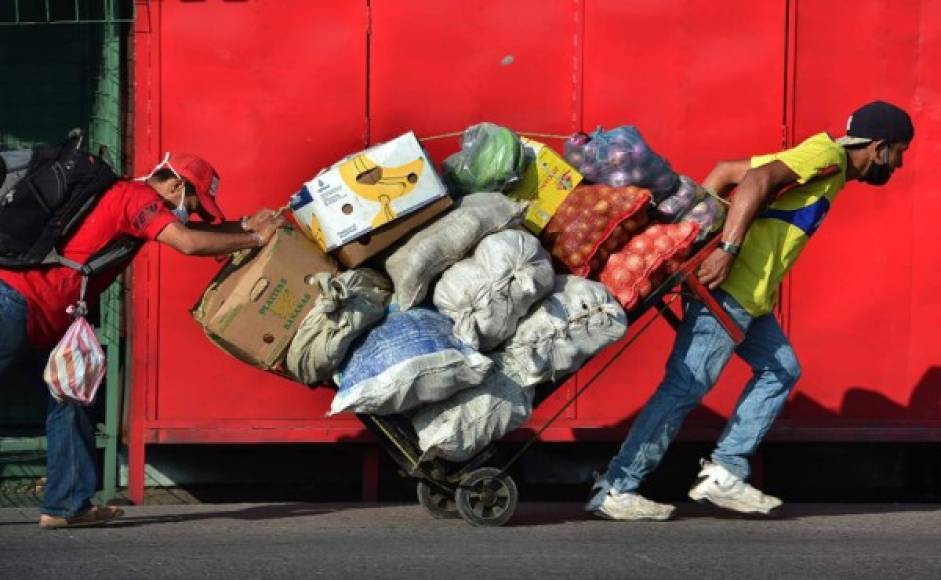 Dos hombres llevan un carro cargado de productos frescos en una calle de Tegucigalpa. Foto AFP