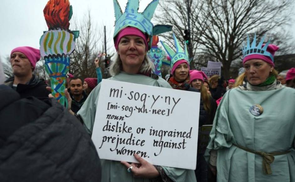 Una mujer vestida de la estatua de la libertad sostiene un cartel que explica el significado de la palabra misógino.