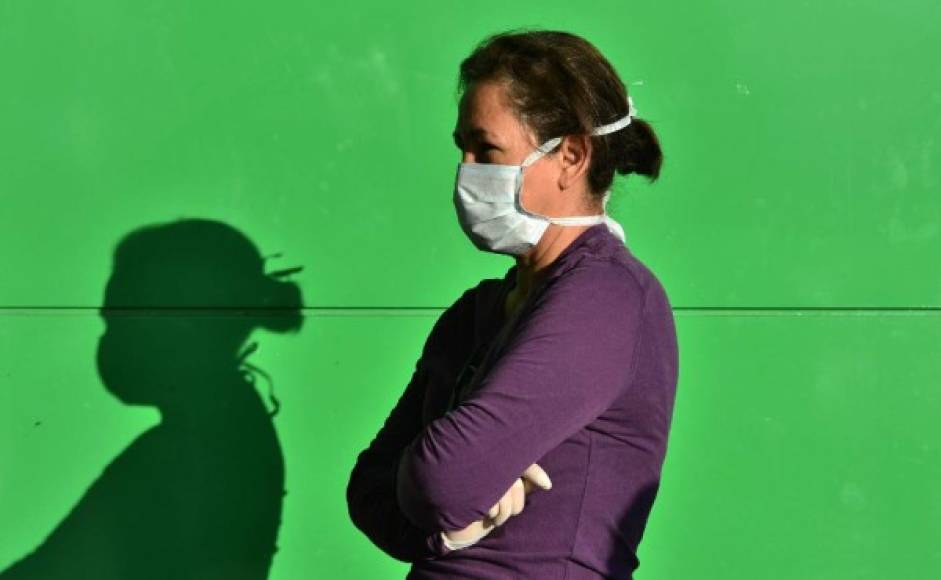 Una mujer usa una máscara facial y guantes mientras hace cola frente a un supermercado durante un descanso del toque de queda impuesto por el gobierno contra la propagación del nuevo coronavirus, en Tegucigalpa, el 19 de marzo de 2020.