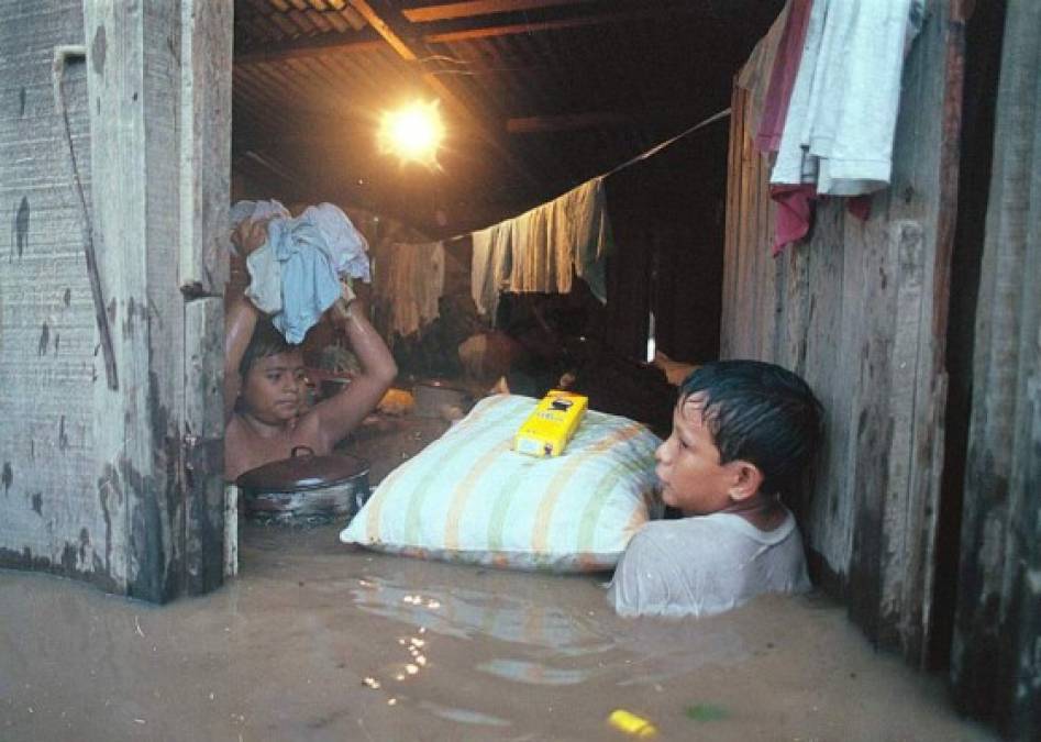 En la imagen, unos niños corren el riesgo de sacar algunas pertenencias de su casa que ya está inundada.