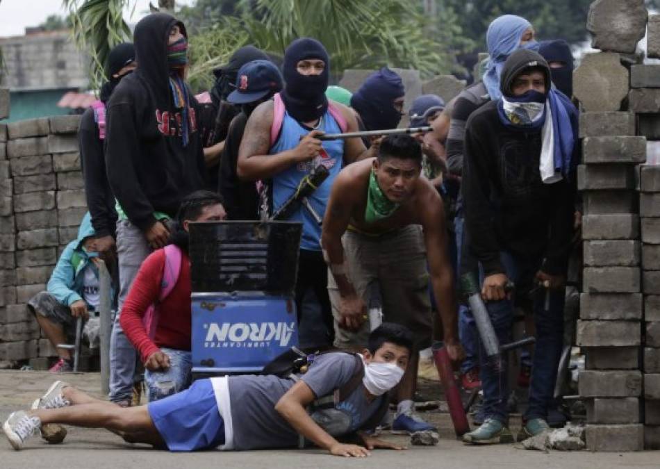Anti-government demonstrators take cover behind a barricade, during clashes with riot police and members of the Sandinista youth, in Masaya some 35 km from Managua on June 19, 2018.<br/>Nicaraguan police and pro-government paramilitaries moved to reassert control over the city of Masaya by force Tuesday after residents of the opposition bastion declared themselves in rebellion against President Daniel Ortega. / AFP PHOTO / INTI OCON
