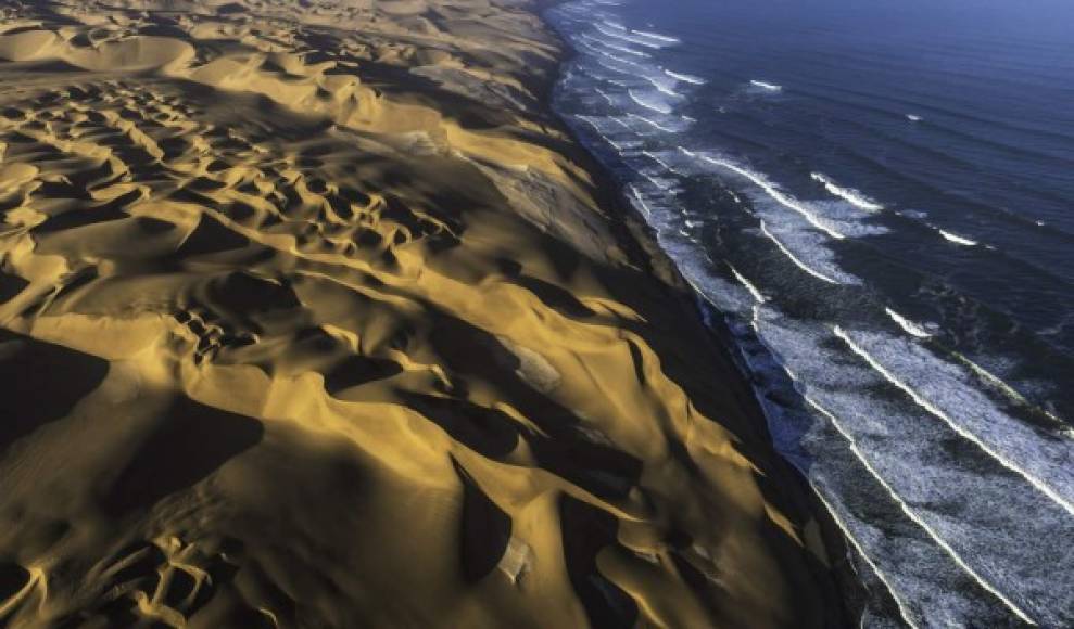 Vista aérea de las dunas de arena en el desierto de Namib colisionando con el Océano Atlántico, Namibia.
