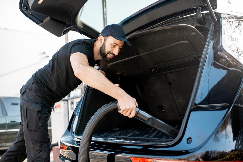 Professional cleaner in black t-shirt and cap vacuuming trunk of a luxury big car outdoors