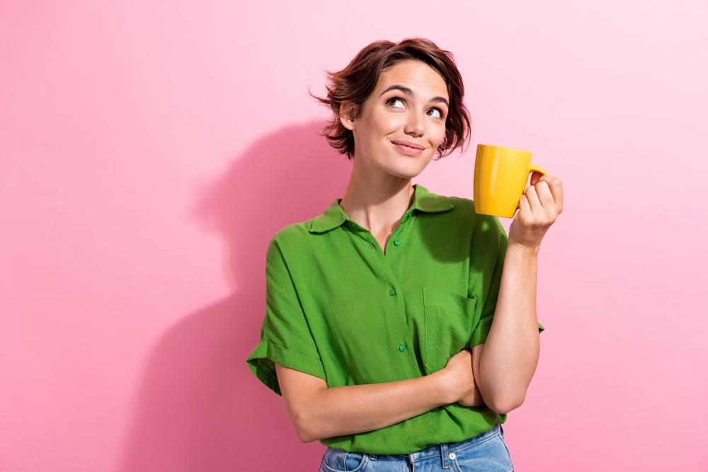 Photo portrait of pretty young girl hold coffee mug look empty space dressed stylish green outfit isolated on pink color background
