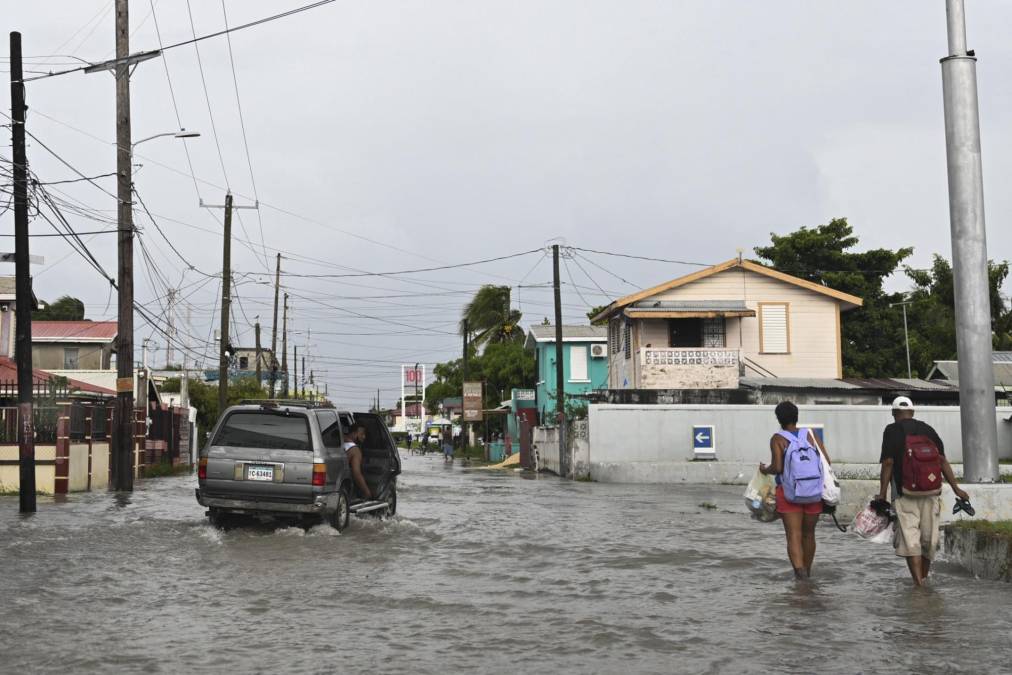 A vehicle and pedestrians make their way through a street flooded due to heavy rains before the arrival of Hurricane Lisa in Belize City on November 2,2022. - The northern part of Central America was on high alert Wednesday for the passage of Hurricane Lisa, with warnings of devastating winds, downpours and flash floods also affecting Mexico's Yucatan peninsula. (Photo by Johan ORDONEZ / AFP)
