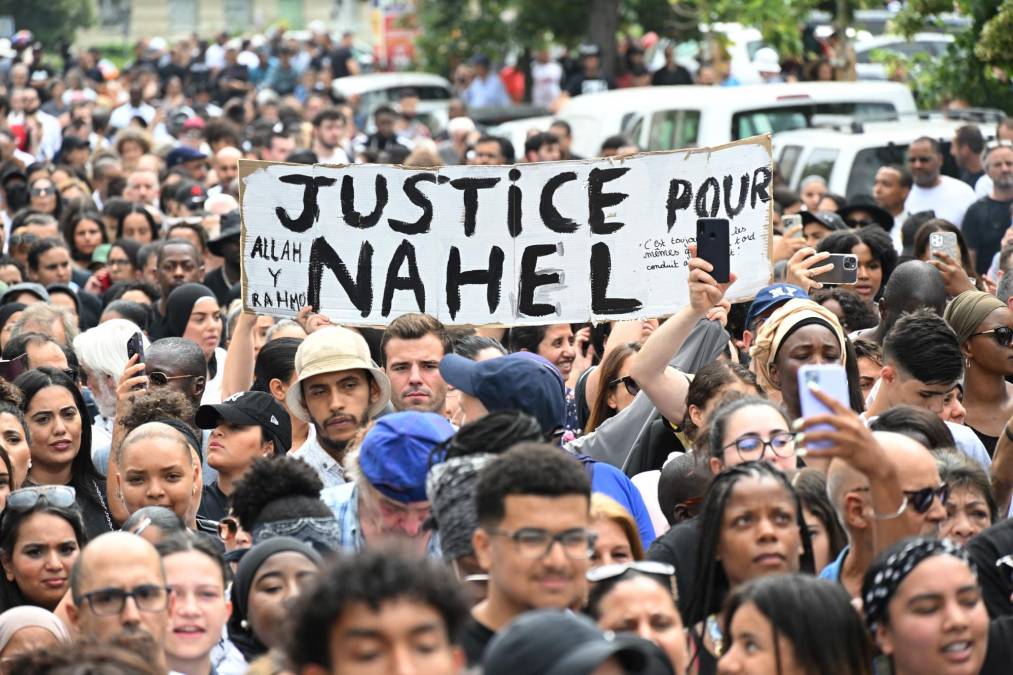 Attendees hold a banner reading "Justice for Nahel", during a commemoration march for a teenage driver shot dead by a policeman, in the Pablo Picasso area of the Parisian suburb of Nanterre, on June 29, 2023. Violent protests broke out in France in the early hours of June 29, 2023, as anger grows over the police killing of a teenager, with security forces arresting 150 people in the chaos that saw balaclava-clad protesters burning cars and setting off fireworks. Nahel M., 17, was shot in the chest at point-blank range in Nanterre in the morning of June 27, 2023, in an incident that has reignited debate in France about police tactics long criticised by rights groups over the treatment of people in low-income suburbs, particularly ethnic minorities. (Photo by Bertrand GUAY / AFP)