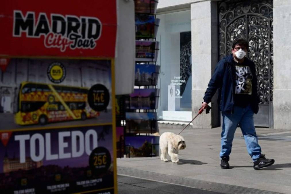 Un hombre con una máscara facial pasea hoy a su perro por Madrid.