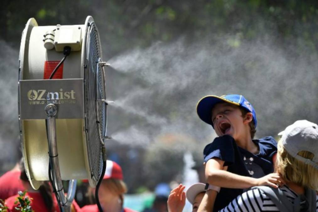 A child is carried in front of a mist fan to cool down from the heat on day one of the Australian Open tennis tournament in Melbourne on January 14, 2019. (Photo by SAEED KHAN / AFP) / -- IMAGE RESTRICTED TO EDITORIAL USE - STRICTLY NO COMMERCIAL USE --