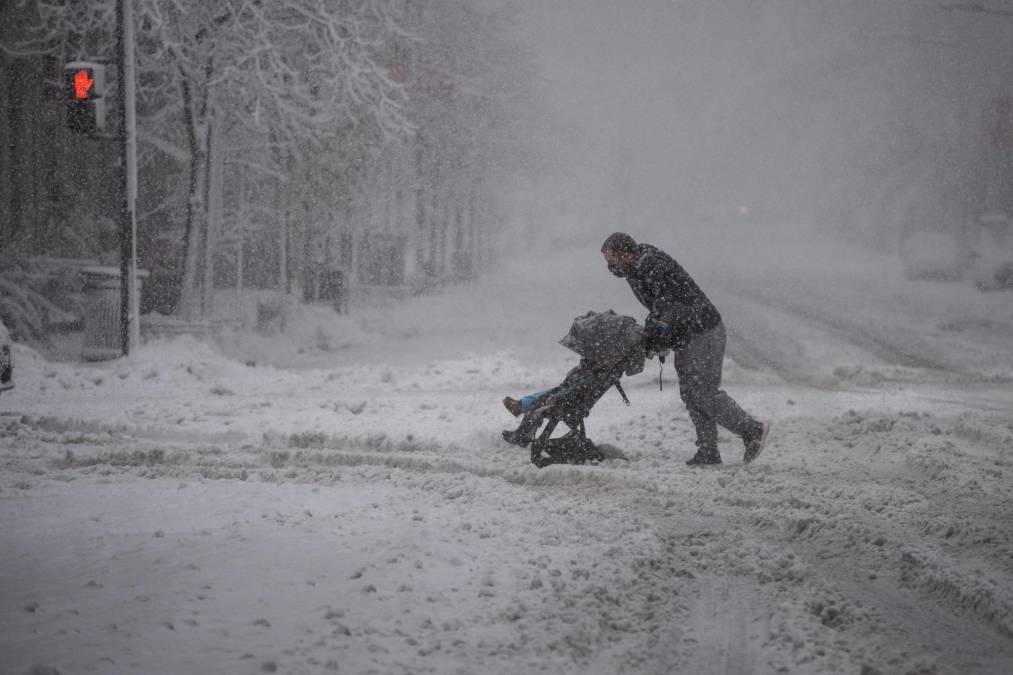  Un hombre intenta cruzar una calle con un cochecito de bebé doble durante una tormenta de nieve en el centro de Washington.