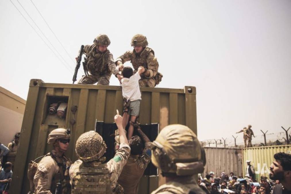 In this image courtesy of the US Central Command Public Affairs, British and Turkish coalition forces, and US Marines assist a child during an evacuation at Hamid Karzai International Airport in Kabul on August 20, 2021. - A Pentagon official confirmed Friday that US evacuation operations from Kabul's airport have been stalling because the receiving base in Qatar is overflowing and could not receive evacuees. 'There has been a considerable amount of time today where there haven't been departures,' Brigadier General Dan DeVoe of the US Air Mobility Command told reporters. (Photo by Victor MANCILLA / US Central Command Public Affairs / AFP) / RESTRICTED TO EDITORIAL USE - MANDATORY CREDIT 'AFP PHOTO / US Marine Corps / Staff Sgt. Victor Mancilla' - NO MARKETING - NO ADVERTISING CAMPAIGNS - DISTRIBUTED AS A SERVICE TO CLIENTS