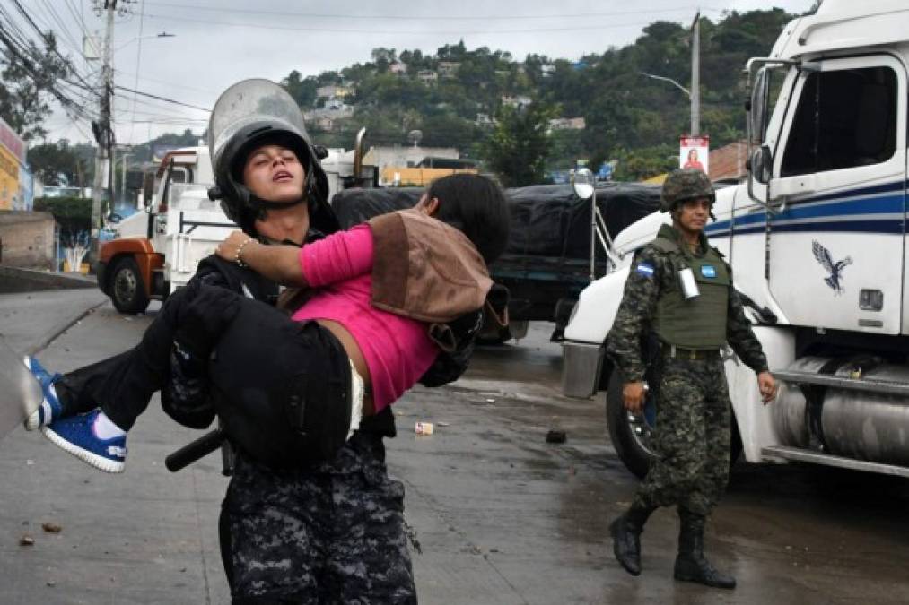 A riot police officer helps a disabled woman affected by tear gas during clashes with supporters of opposition candidate Salvador Nasralla in Tegucigalpa, on December 18, 2017.<br/>Honduran President Juan Orlando Hernandez is declared the winner of a heavily disputed presidential election held three weeks ago, despite mounting protests and opposition claims of fraud. / AFP PHOTO / ORLANDO SIERRA