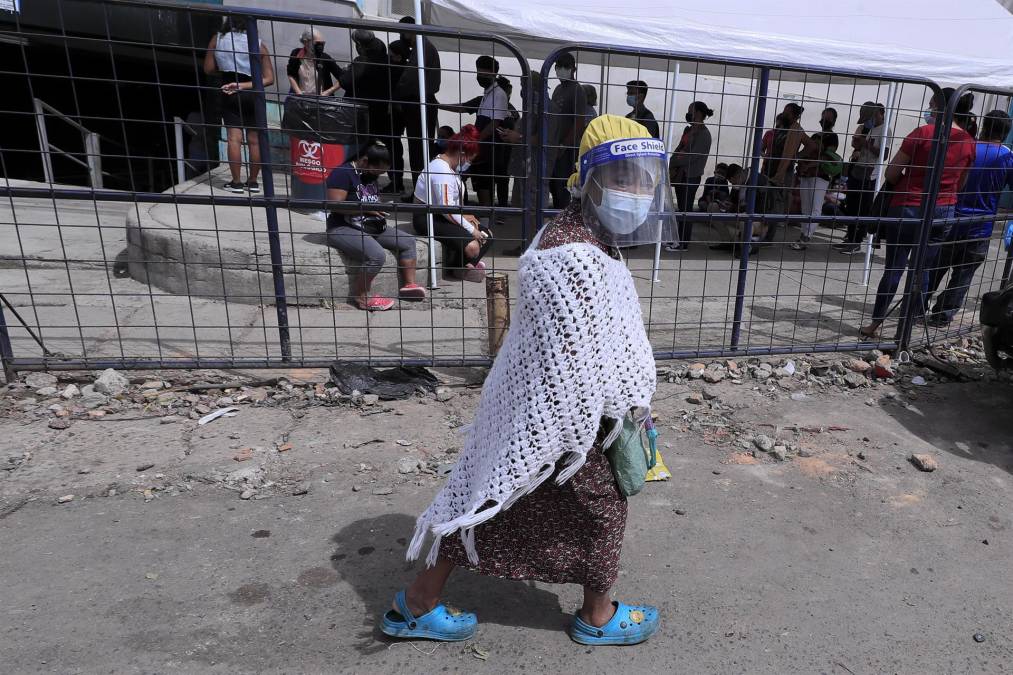 Una mujer camina con una careta protectora frente a personas que hacen fila en un centro de triaje de detección temprana del coronavirus este jueves, en Tegucigalpa. 