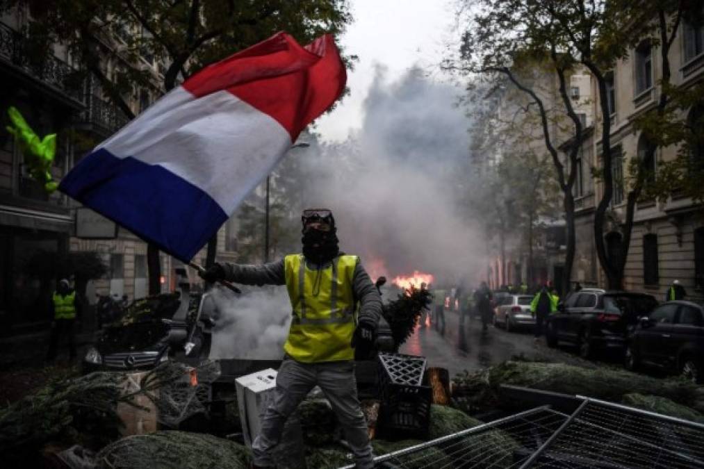 A demonstrator holds a French flag during a protest of Yellow vests (Gilets jaunes) against rising oil prices and living costs, on December 1, 2018 in Paris. - Speaking at the Paris police's command centre, French Prime Minister said 36,000 people were protesting across France, including 5,500 in the capital for this 3rd nationwide day of blockade ands demos. (Photo by Alain JOCARD / AFP)