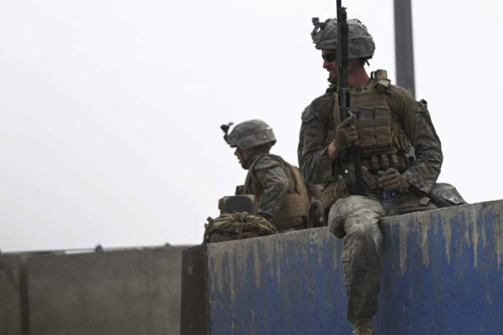 US soldiers sit on a wall as Afghans gather on a roadside near the military part of the airport in Kabul on August 20, 2021, hoping to flee from the country after the Taliban's military takeover of Afghanistan. (Photo by Wakil KOHSAR / AFP)