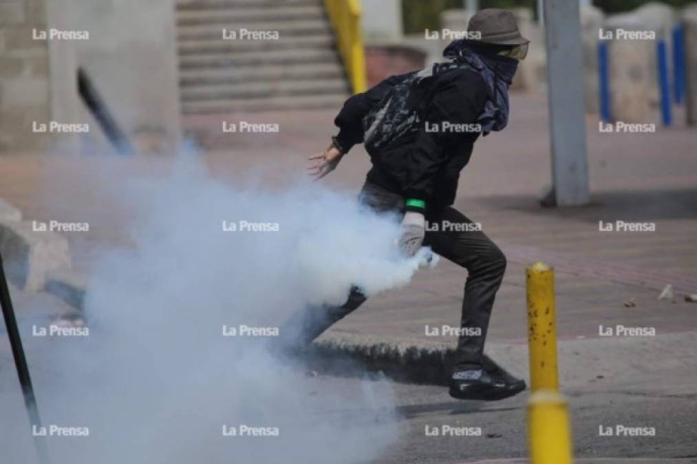 Un joven toma una bomba lacrimógena para devolverla a la Policía.