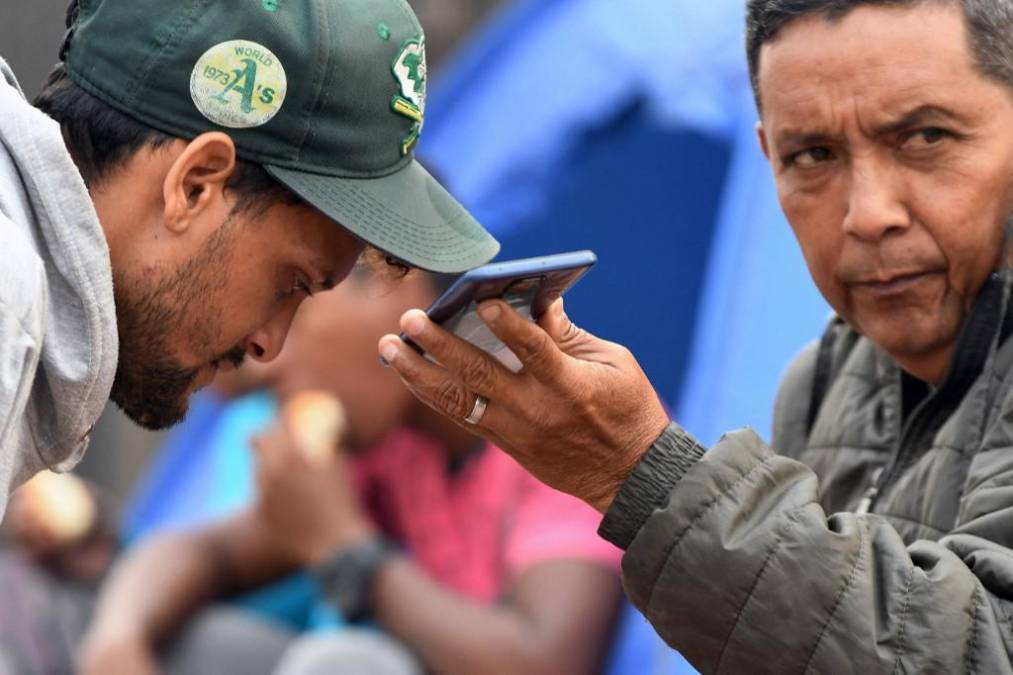  Migrantes venezolanos hablan con familiares en un teléfono móvil mientras esperan afuera del Banco Central de Honduras para retirar dinero para continuar su viaje a los Estados Unidos.