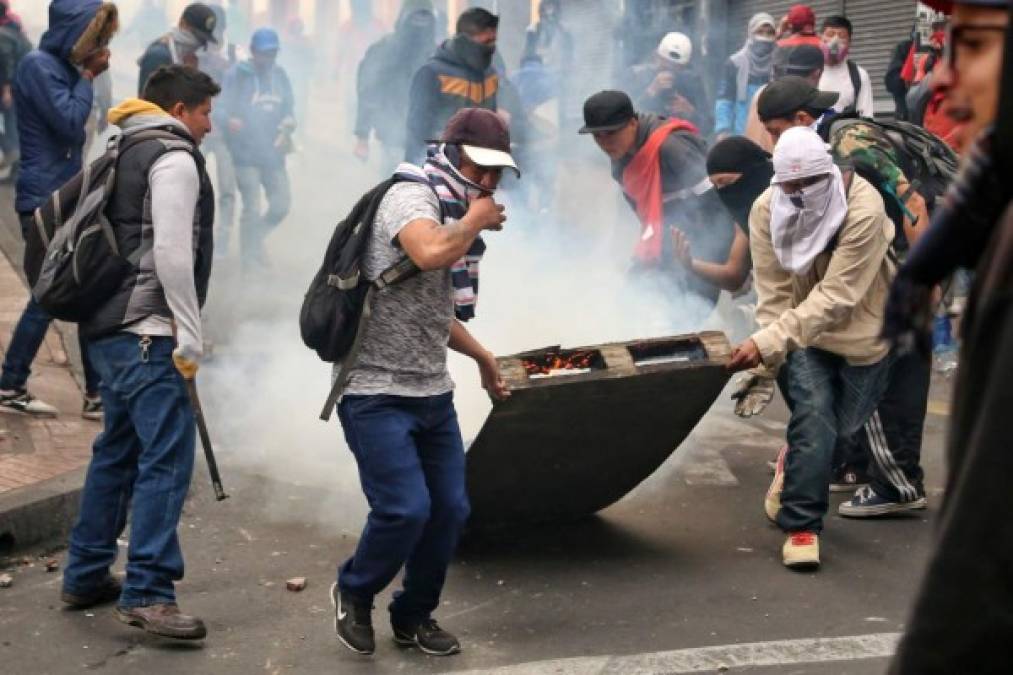 Demonstrators pull a pallet on fire during clashes in Quito on October 7, 2019 following days of protests against the sharp rise in fuel prices sparked by authorities' decision to scrap subsidies. - Ecuador has been rocked by days of demonstrations in response to increases of up to 120 percent in fuel prices, which came into force on Thursday after the government scrapped subsidies as part of an agreement signed in March with the International Monetary Fund (IMF) to obtain loans despite its high public debt. (Photo by Cristina VEGA / AFP)