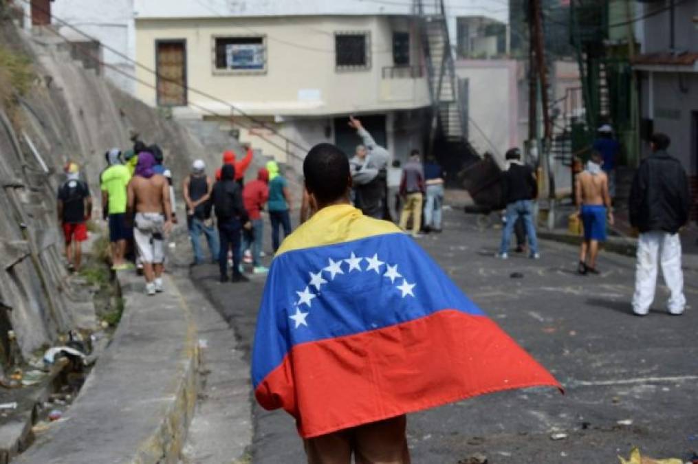 An anti-government demonstrator is wrapped in a Venezuelan national flag during clashes with police and troops in the surroundings of a National Guard command post in Cotiza, in northern Caracas, on January 21, 2019. - A group of soldiers rose up against Venezuela's President Nicolas Maduro at a command post in northern Caracas on Monday, but were quickly arrested after posting an appeal for public support in a video, the government said. (Photo by Federico PARRA / AFP)