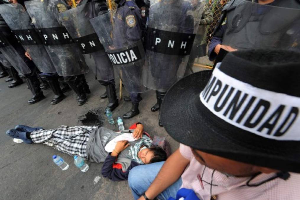 Un indignado en huelga de hambre se tira en el suelo junto a los policías en los alrededores de la Casa Presidencial en Tegucigalpa. AFP
