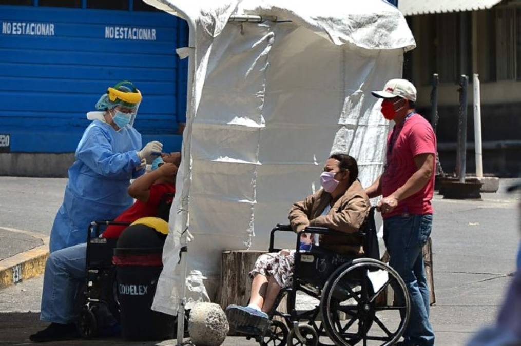 Un trabajador de salud recolecta una muestra de hisopo nasal de un paciente para analizar el COVID-19 en una de las cuatro carpas instaladas en el estacionamiento del Hospital Escuela. AFP