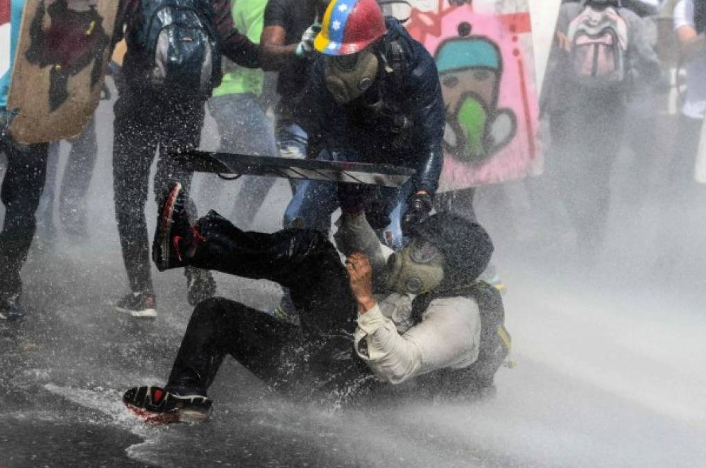 Un manifestante cae tras ser rociado con un cañón de agua.