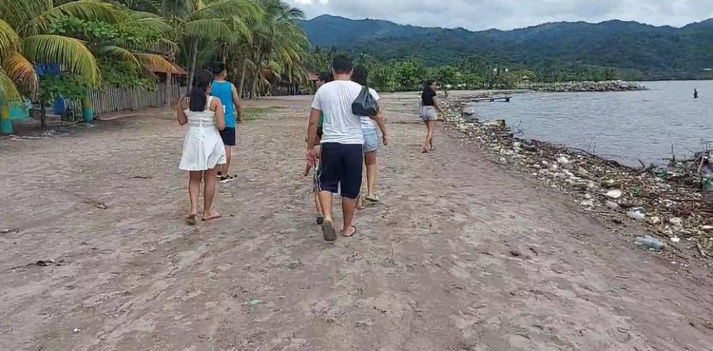 Un grupo de turistas camina a la orilla de la playa, la cual estaba llena de desechos.