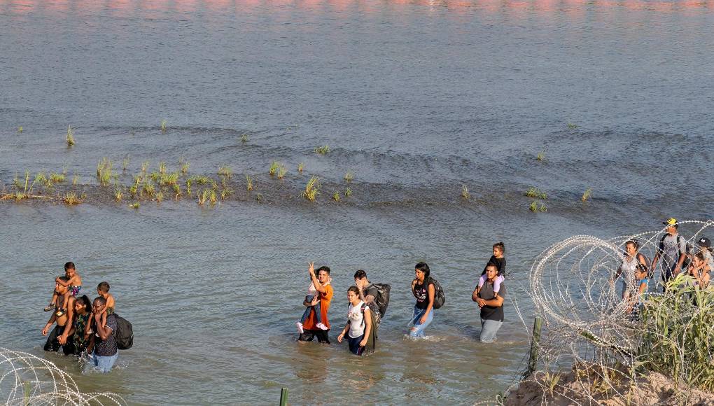 (FILES) Migrants walk between Concertina wire and a string of buoys placed on the water along the Rio Grande border with Mexico in Eagle Pass, Texas, on July 16, 2023, to prevent illegal immigration entry to the US. The US Supreme Court lifted its hold March 19, 2024 on a controversial Texas law that would allow state police to arrest and deport migrants who cross illegally into the United States from Mexico. (Photo by SUZANNE CORDEIRO / AFP)