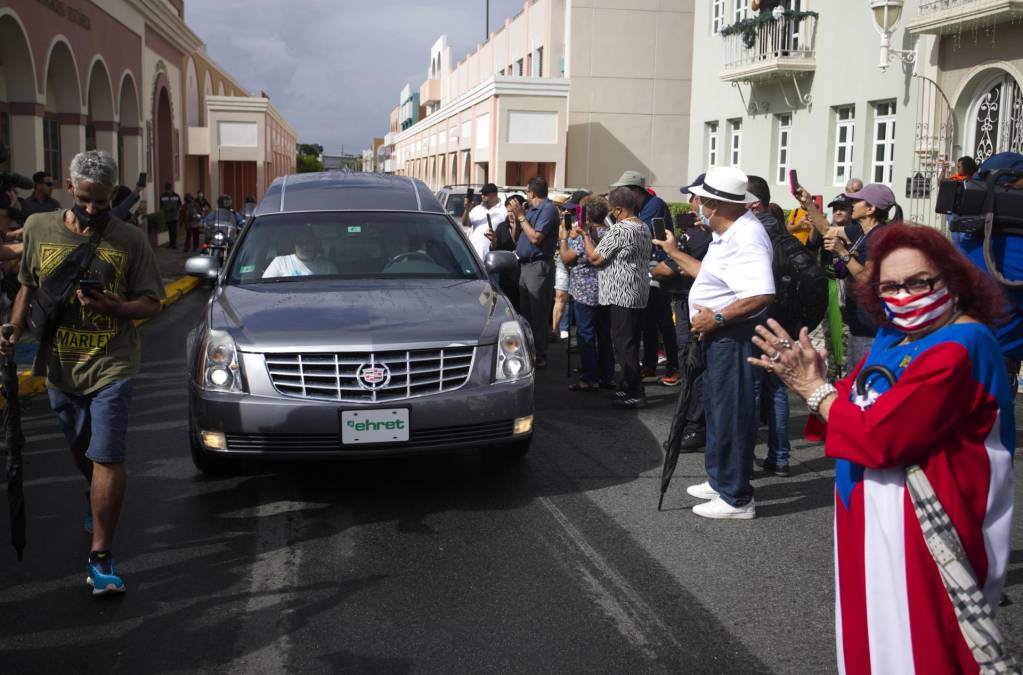 Varias personas observan el paso de la carroza fúnebre que carga el ataúd del salsero puertorriqueño Lalo Rodríguez, hoy, en Carolina (Puerto Rico).