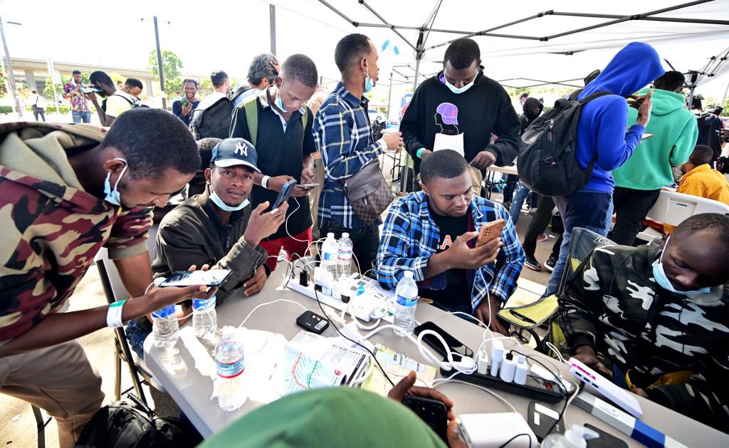 Migrantes de Texas cargan sus teléfonos celulares después de ser dejados en una estación de tren en San Diego, California.