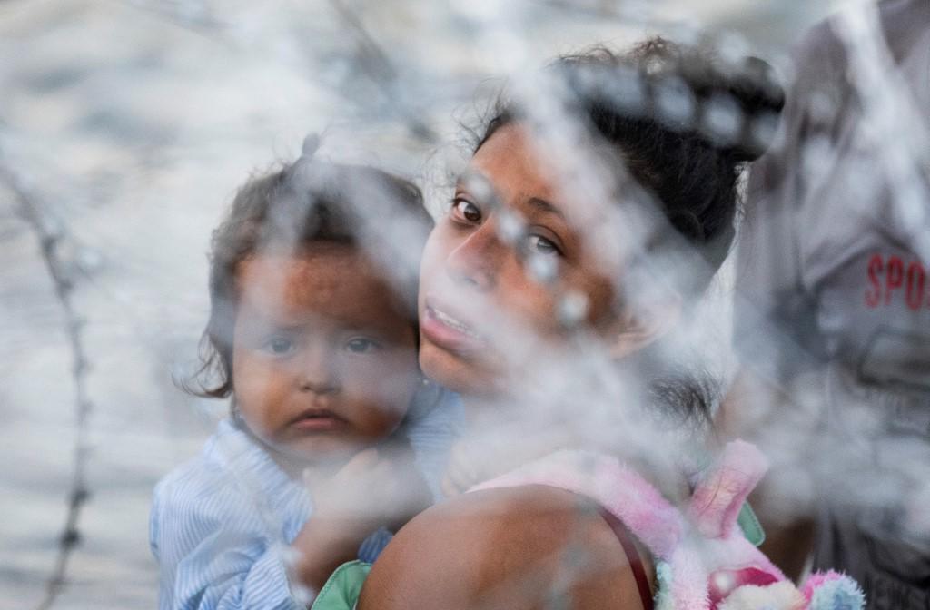 Una madre carga a su hijo en la frontera entre México y Estados Unidos.