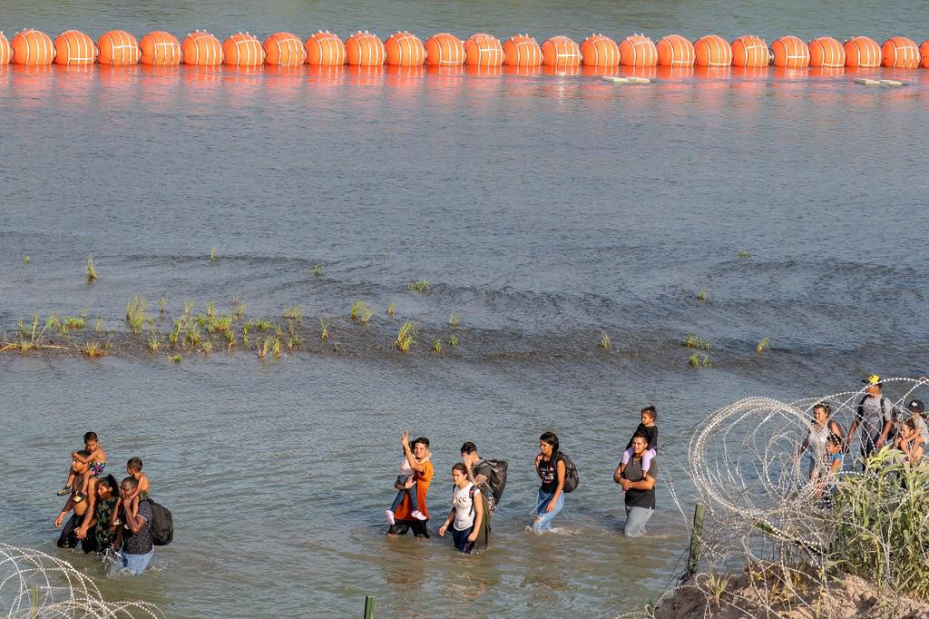 Migrantes caminan entre el alambre Concertina y una serie de boyas colocadas en el agua a lo largo de la frontera del Río Grande con México en Eagle Pass, Texas.