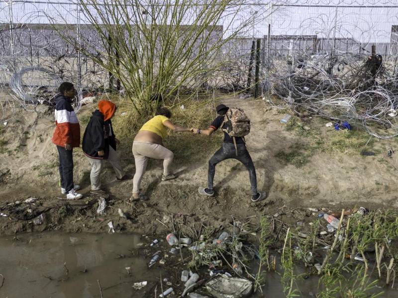 Un grupo de migrantes intenta cruzar una alambrada tras atravesar el río Bravo en el sur de Texas.