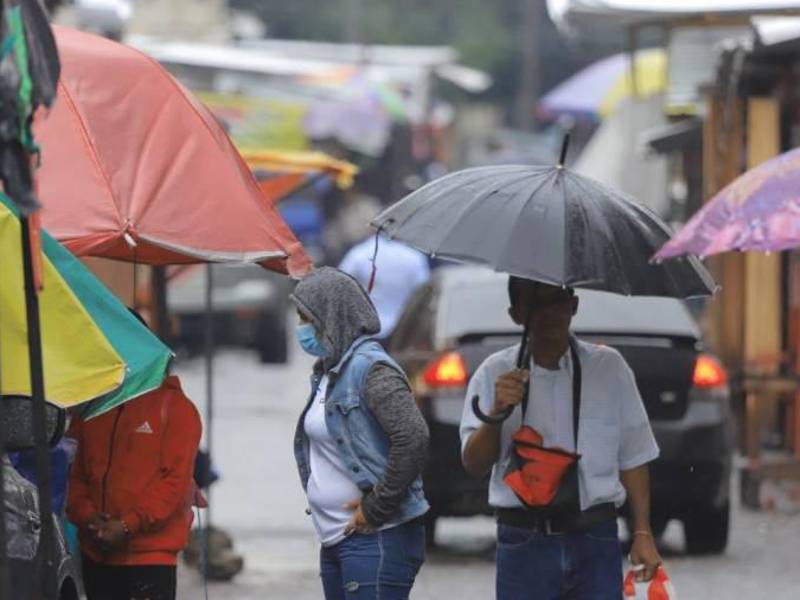 Hondureños caminan por el centro de San Pedro Sula mientras llueve.