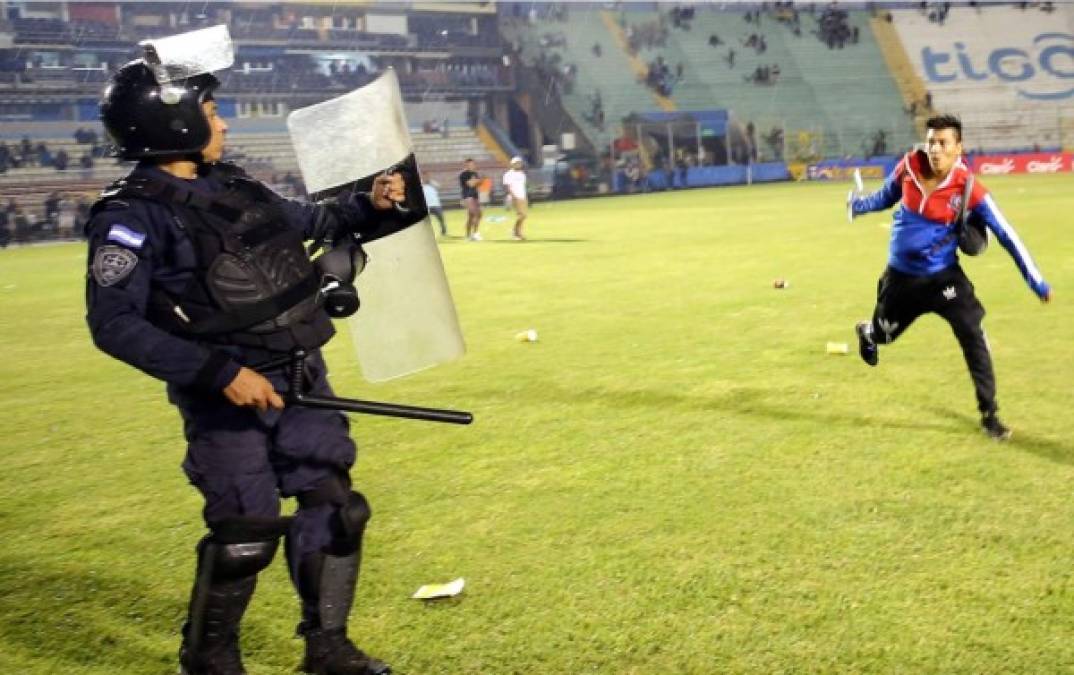 Un policía trata de protegerse de la agresión de un aficionado del Olimpia en la cancha del estadio Nacional.