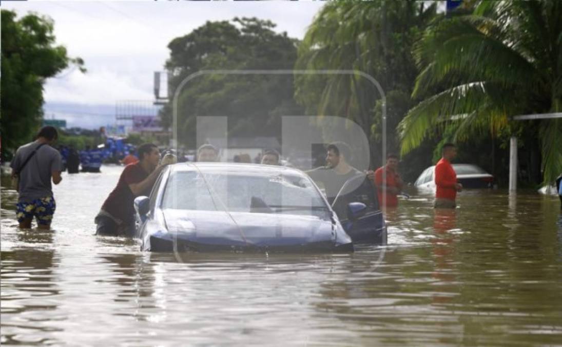 Ciudadanos halando un vehículo casi cubierto por el agua tras intensas lluvias.