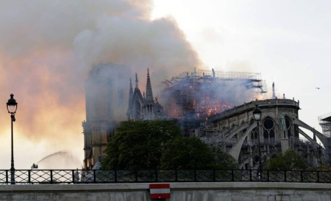 Un bombero usa una manguera para apagar las llamas y el humo que sale del techo de la catedral de Notre-Dame.