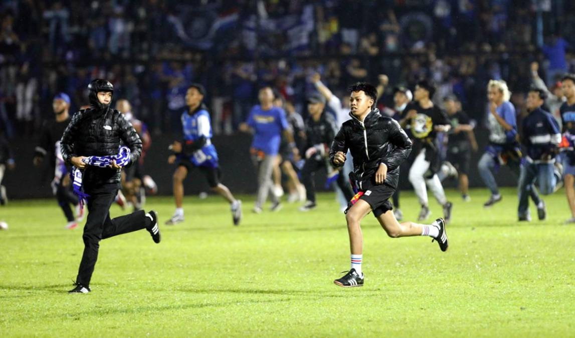 Aficionados al futbol corren durante una serie de enfrentamientos en el estadio Kanjuruhan de Malang, Indonesia.