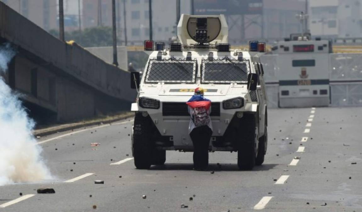 Un manifestante se enfrenta a pie ante las fuerza bolivarianas del orden, que se conducen en un blindado.