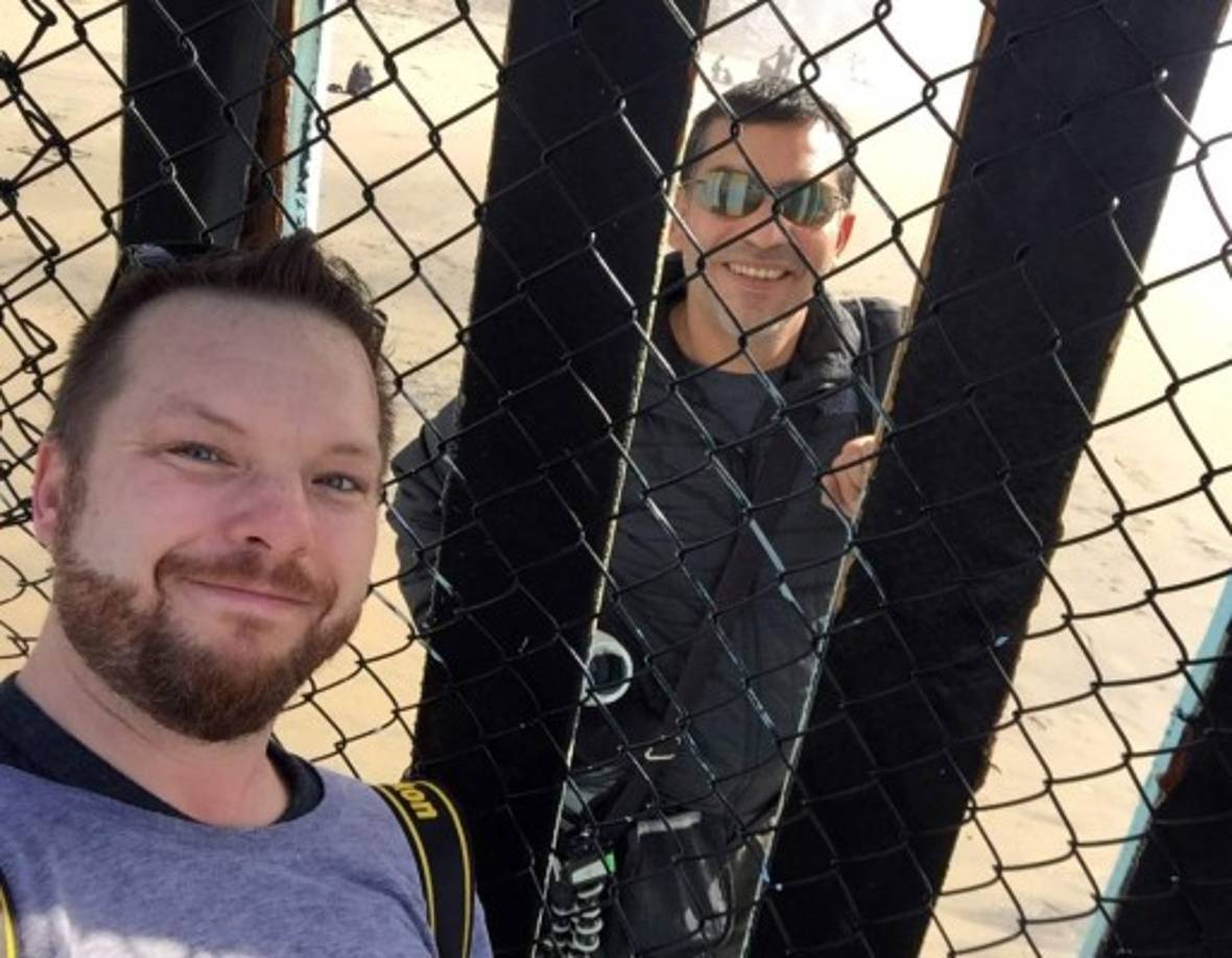 Un turista estadounidense posa en el muro que divide a San Diego y Tijuana con un ciudadano mexicano del otro lado.<br/>