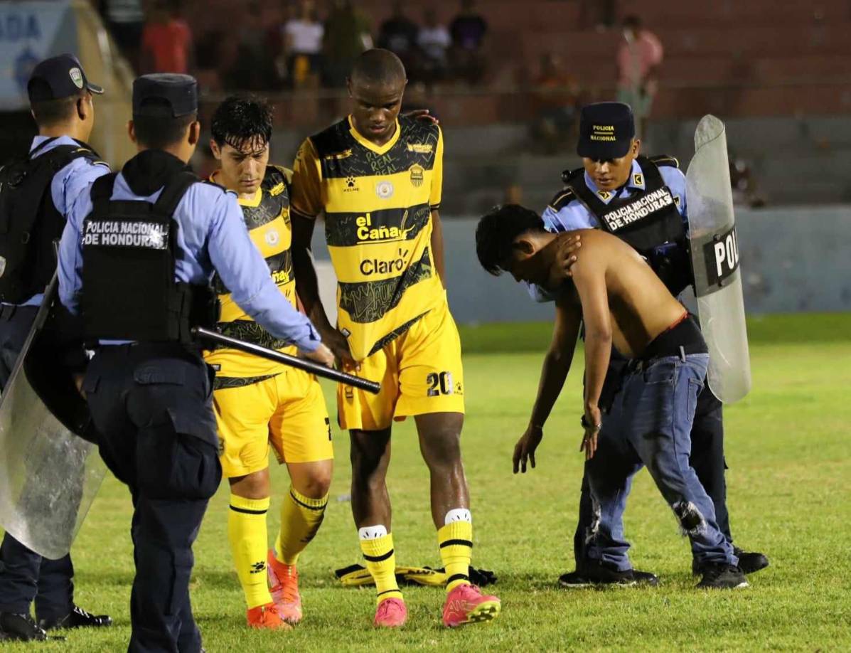 El panorama del rostro cabizbajo de los futbolistas de Real España ante la detención del aficionado en el terreno de juego.