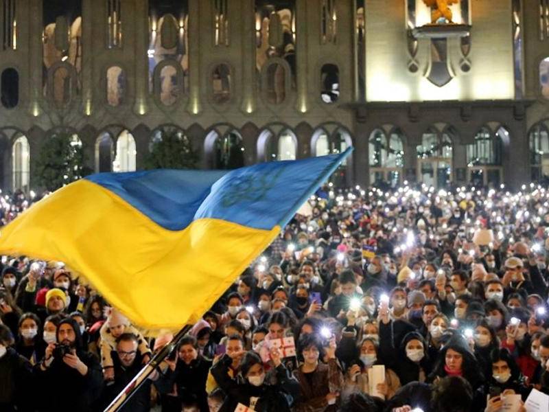 Manifestantes con antorchas encendidas mientras se ondea una bandera ucraniana durante una manifestación en apoyo al país invadido por Rusia.
