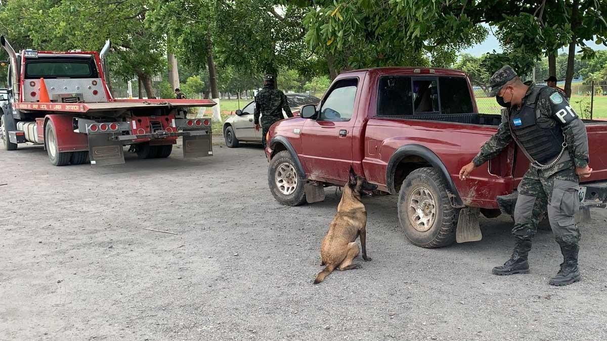 Un agente de la Policía Militar, junto a su perro, inspeccionan uno de los vehículos decomisados.