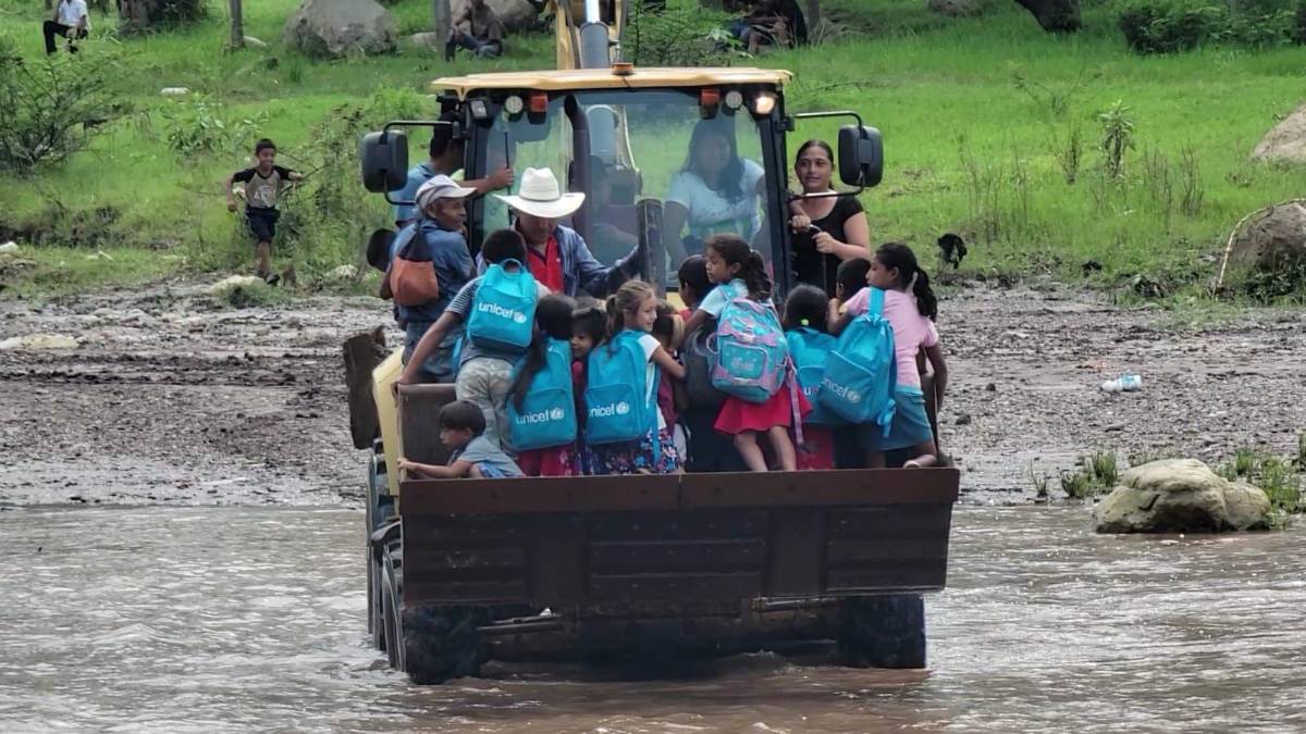 Estudiantes pasan el río en una retroexcavadora.