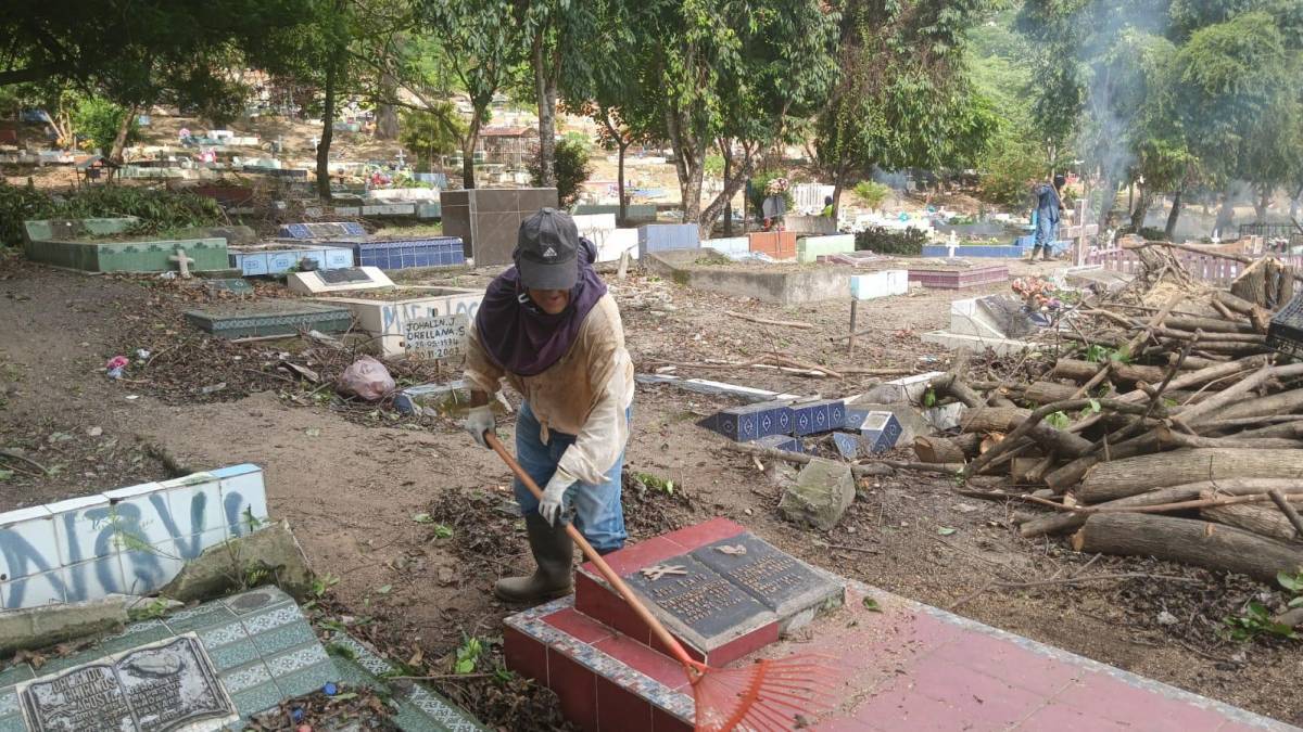 Un jornalero limpia una tumba en el cementerio de la Rivera Hernández.