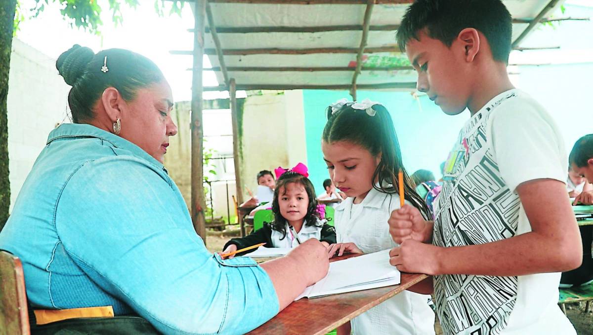 La maestra Elizabeth Bojorquez revisa las tareas a los niños de primer grado bajo la “champa”.